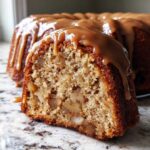 Close-up of a slice of moist apple bundt cake filled with chunks of apple and topped with dripping caramel glaze.