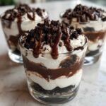 Close-up of an individual Baileys Chocolate Cheesecake Trifle layered with cream, chocolate, and topped with cookie crumbs and drizzle.