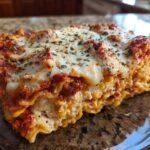 Close-up of a hearty slice of baked ravioli comfort casserole with melted cheese and herbs.