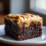 Close-up of a dense, dark chocolate banana bread brownies square topped with thick peanut butter frosting.