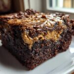 Close-up of a rich, fudgy banana bread brownies square with a gooey peanut butter swirl on top, served on a white plate.