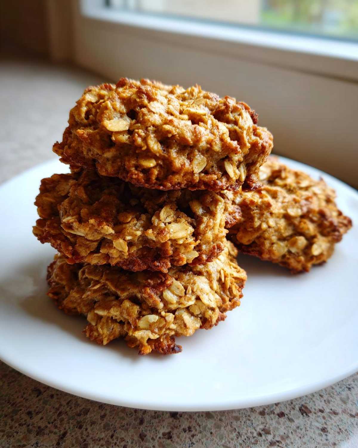 A stack of four golden brown banana oatmeal cookies piled on a white plate.
