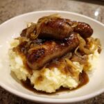 Close-up of delicious bangers and mash topped with rich gravy and caramelized onions.