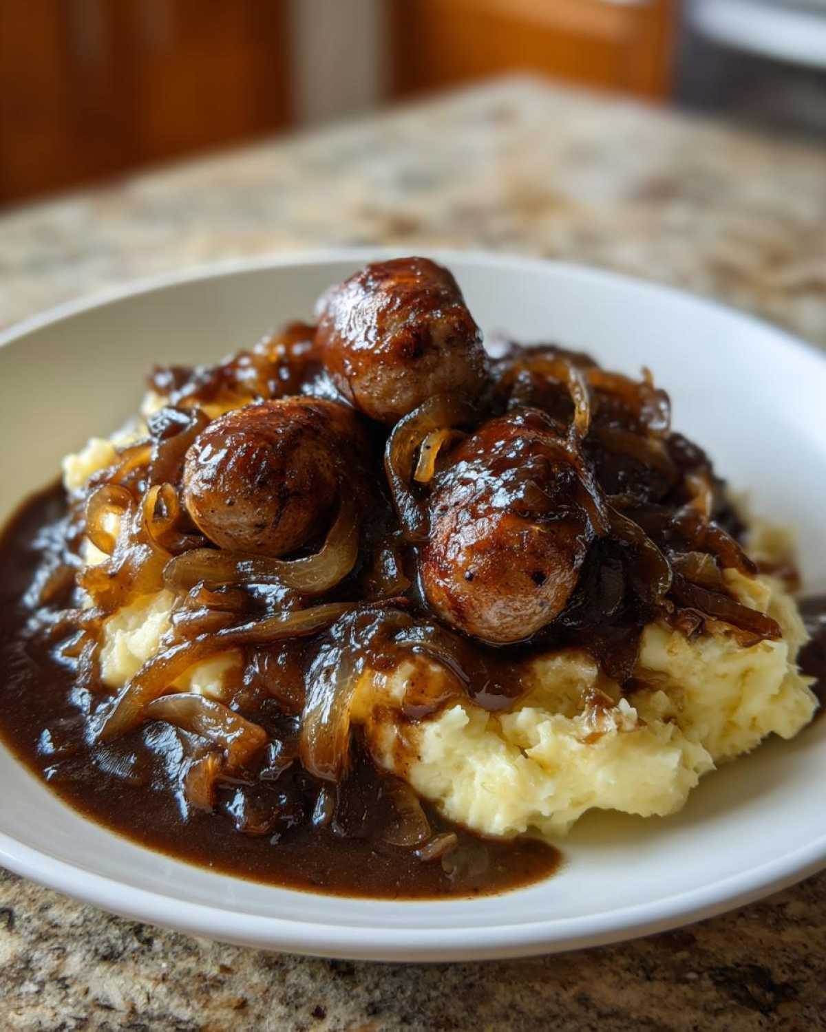A close-up of delicious bangers and mash topped with caramelized onions and dark, rich gravy.