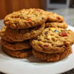 A close-up stack of chewy fruitcake cookies loaded with colorful dried fruit and nuts, featured prominently on a white plate.
