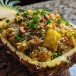 Close-up of delicious pineapple fried rice served inside a hollowed-out pineapple half, topped with cashews and green onions.