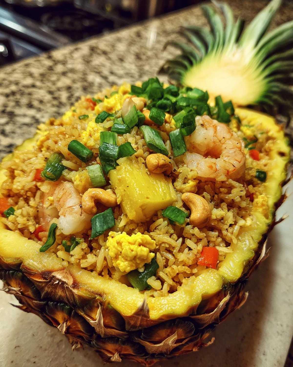 Close-up of vibrant pineapple fried rice served inside a hollowed-out pineapple half, topped with shrimp and cashews.