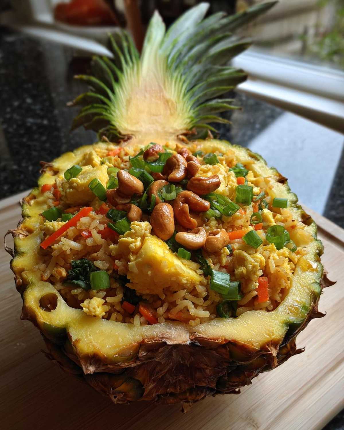Vibrant pineapple fried rice served inside a hollowed-out pineapple half, topped with cashews and green onions.