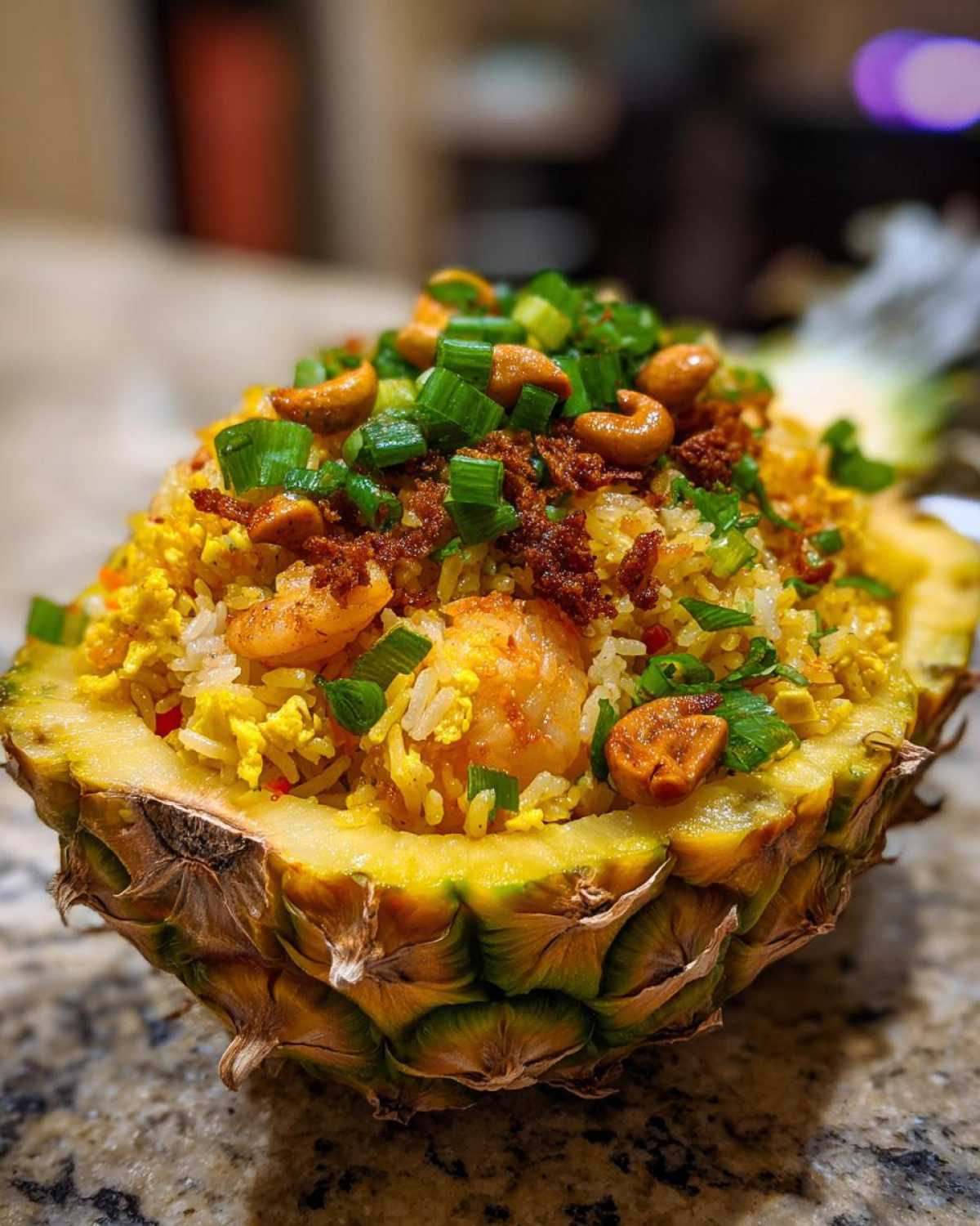 Close-up of flavorful pineapple fried rice served inside a hollowed-out pineapple shell, topped with shrimp, cashews, and green onions.