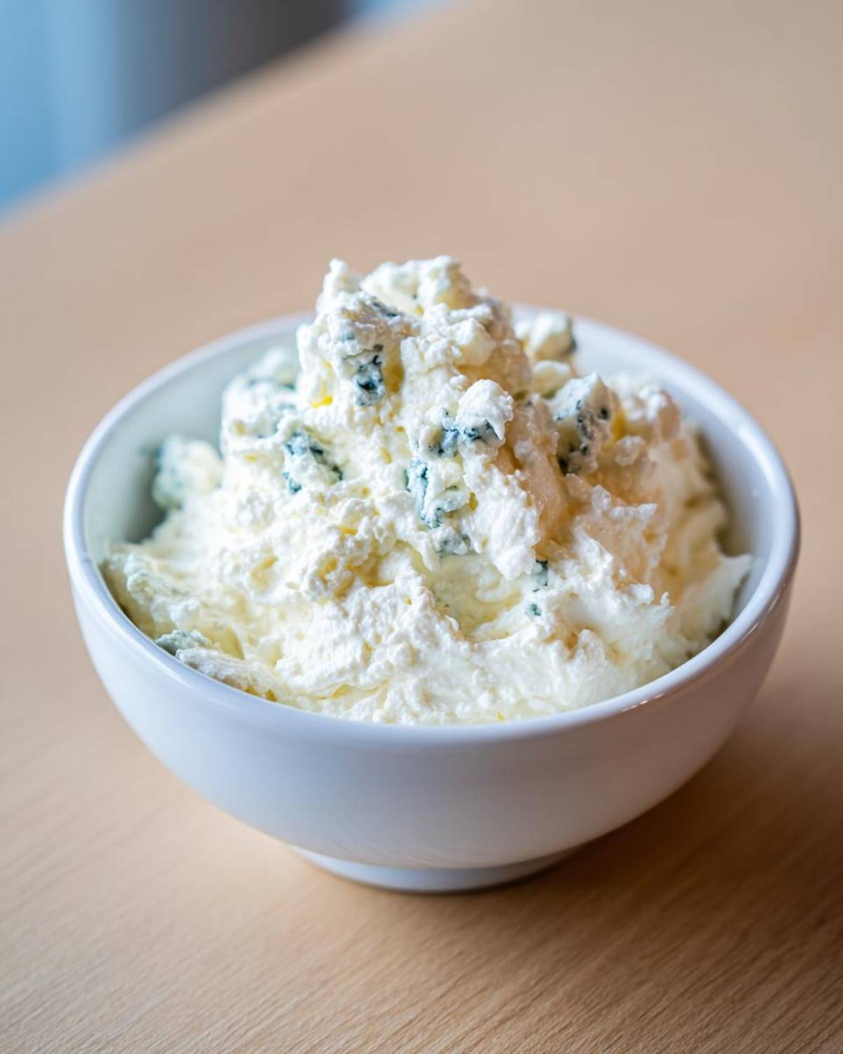 A close-up of chunky, homemade blue cheese dip generously piled in a small white bowl.