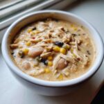 Close-up of a hearty bowl of creamy cream cheese chicken chili filled with shredded chicken, white beans, black beans, and corn.