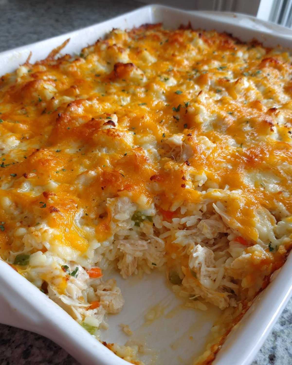A close-up of a baked chicken and rice casserole topped with melted, bubbly cheddar cheese.