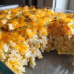 A close-up view of a creamy chicken and rice casserole topped with melted cheddar cheese and herbs.
