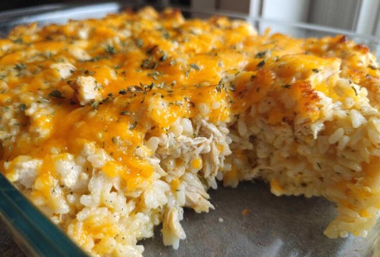 A close-up view of a creamy chicken and rice casserole topped with melted cheddar cheese and herbs.