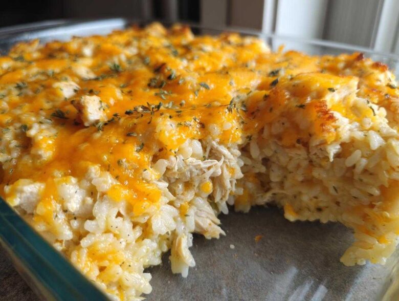 A close-up view of a creamy chicken and rice casserole topped with melted cheddar cheese and herbs.