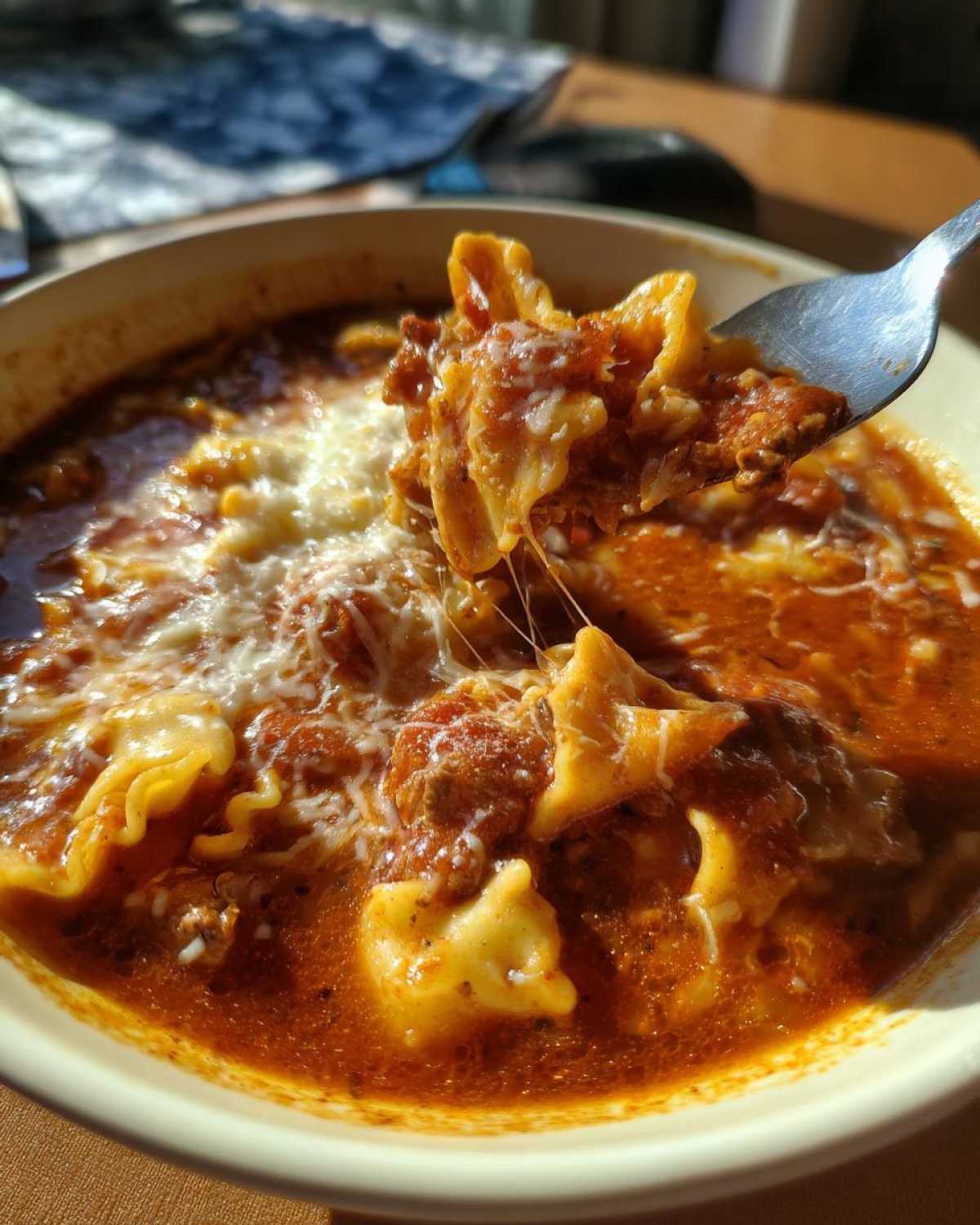 A fork lifts a cheesy, saucy bite of crockpot lasagna soup showing melted mozzarella strings.