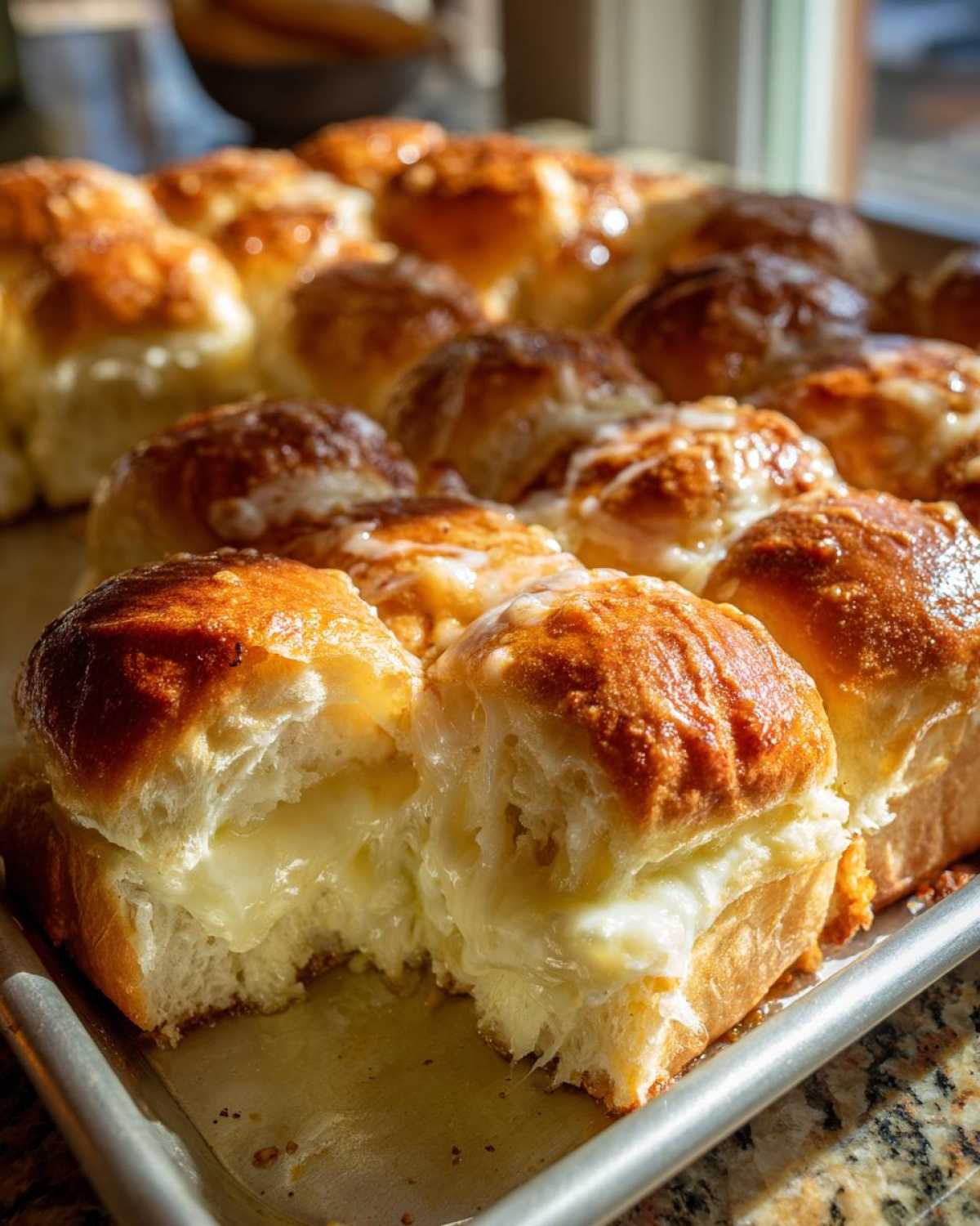 Close-up of freshly baked grinder sliders with golden tops, one pulled apart revealing a gooey, melted cheese filling.