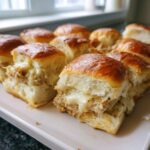 Close-up of several cheesy grinder sliders with golden brown tops served on a white platter.