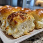 Close-up of cheesy, pull-apart grinder sliders with a golden-brown, bubbly topping on a white platter.