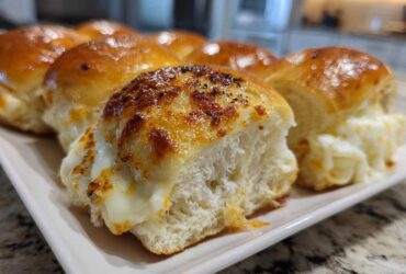 Close-up of cheesy, pull-apart grinder sliders with a golden-brown, bubbly topping on a white platter.