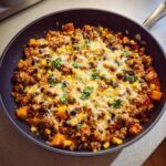 A close-up overhead view of a savory sweet potato skillet topped with melted cheese and fresh cilantro.