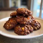 A close-up stack of chewy fruitcake cookies loaded with colorful dried fruit and nuts on a white plate.
