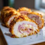 Close-up of a cross-section of golden-brown Chicken Cordon Bleu showing melted cheese and ham filling.