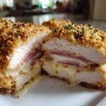 Close-up of a sliced chicken cordon bleu showing crispy breading, ham, and oozing melted Swiss cheese inside the chicken breast.
