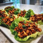 A row of freshly prepared chicken lettuce wraps filled with savory brown sauce and topped with green onions.