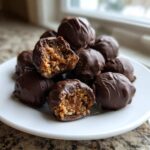 A stack of chocolate-covered pecan pie balls, with two cut in half showing the textured filling.