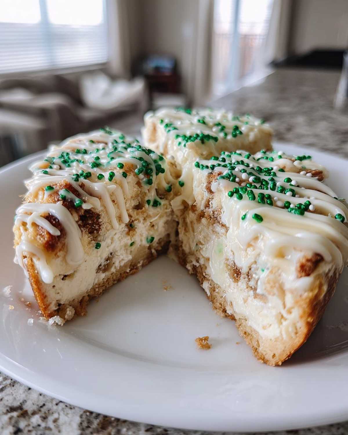 Close-up of a portion of christmas tree cheesecake cut open, showing creamy filling, crust, and white icing with green sprinkles.