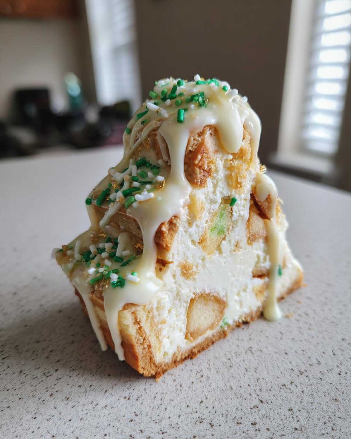 A slice of tiered christmas tree cheesecake topped with white glaze and green sprinkles.