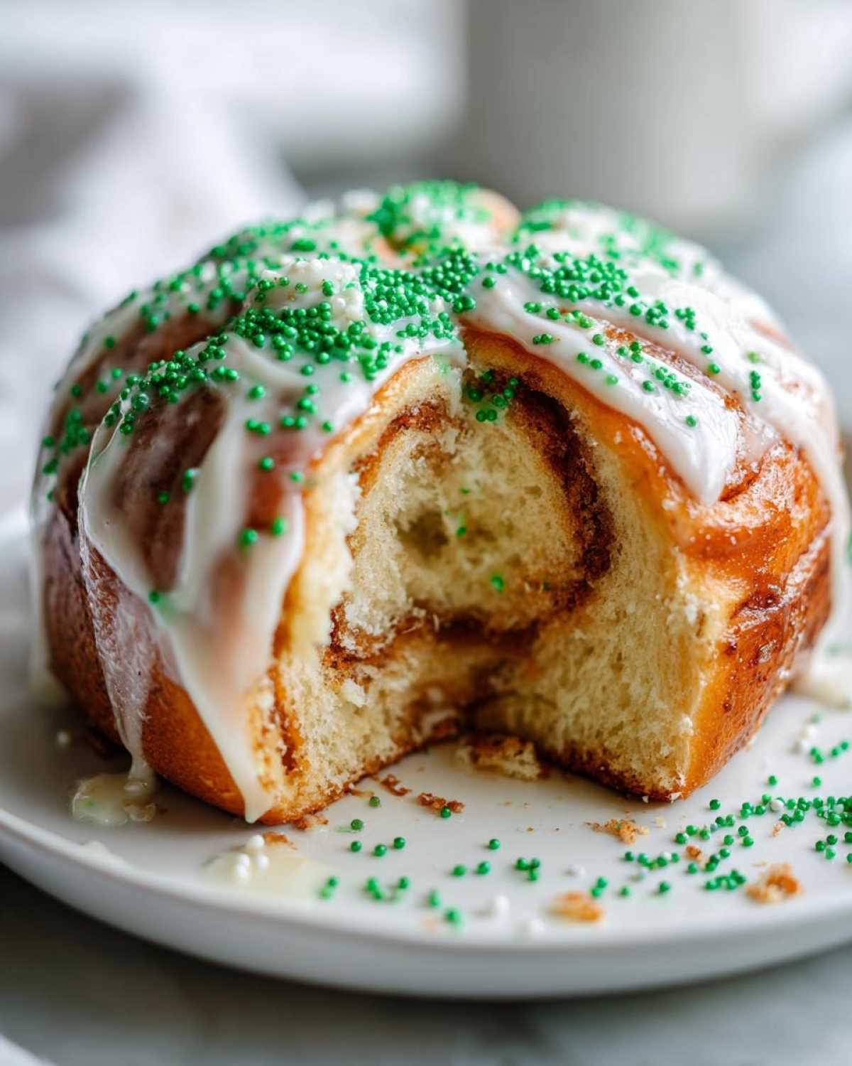 A single serving of Christmas tree cinnamon rolls, cut open to show the swirl, topped with white icing and green sprinkles.