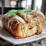 A close-up of a section of Christmas tree cinnamon rolls, drizzled with white icing and topped with bright green sprinkles.
