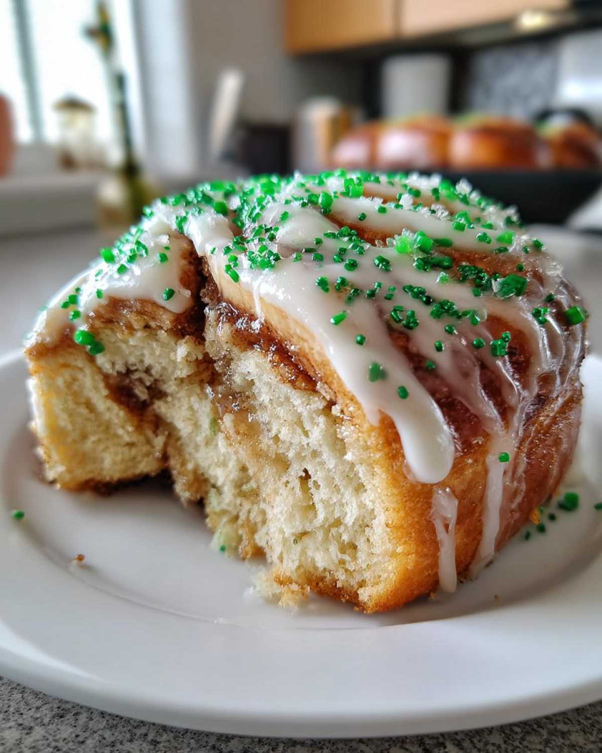 A close-up view of a soft, gooey Christmas tree cinnamon roll topped with white icing and green sprinkles.