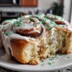 Close-up of freshly baked Christmas tree cinnamon rolls topped with white icing and bright green sprinkles.