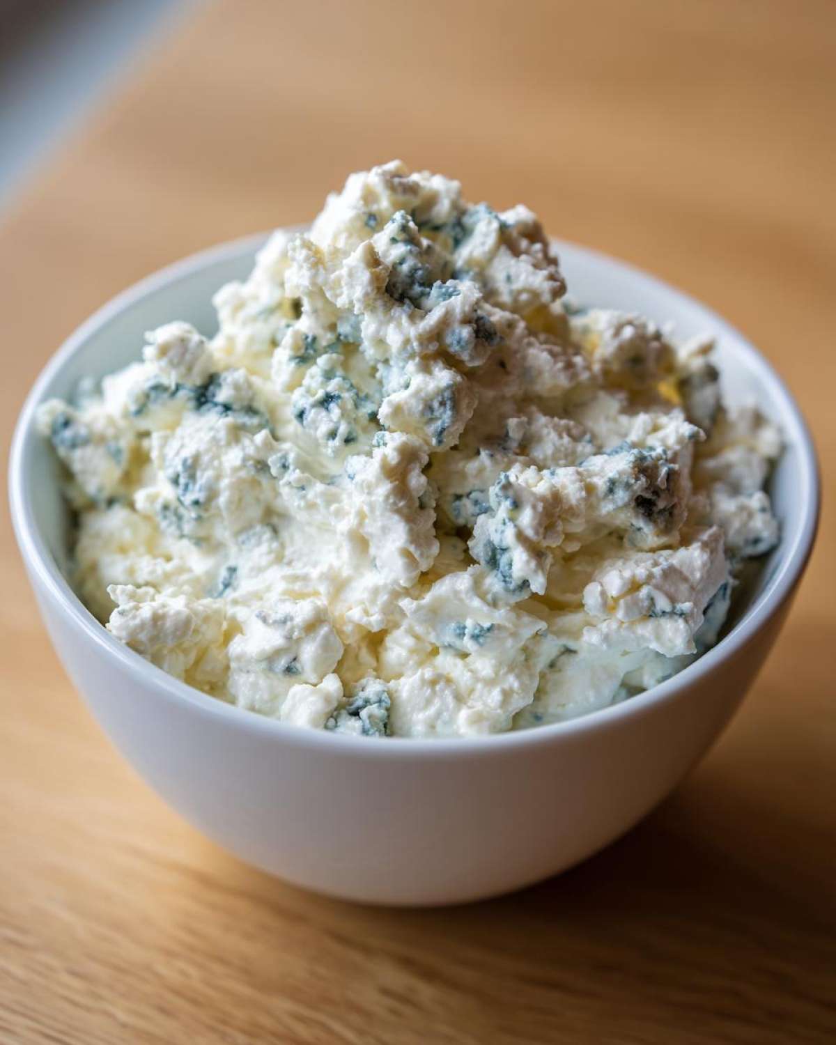 Close-up of chunky, crumbly blue cheese dip mixture in a white bowl, showcasing the blue veining.