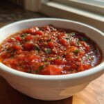 A white bowl filled with chunky, vibrant homemade pizza sauce, seasoned with herbs and pepper flakes.