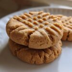 Close-up of three classic peanut butter cookies stacked on a white plate, showing the traditional criss-cross fork marks.