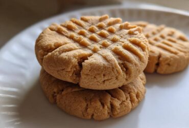 Close-up of three classic peanut butter cookies stacked on a white plate, showing the traditional criss-cross fork marks.