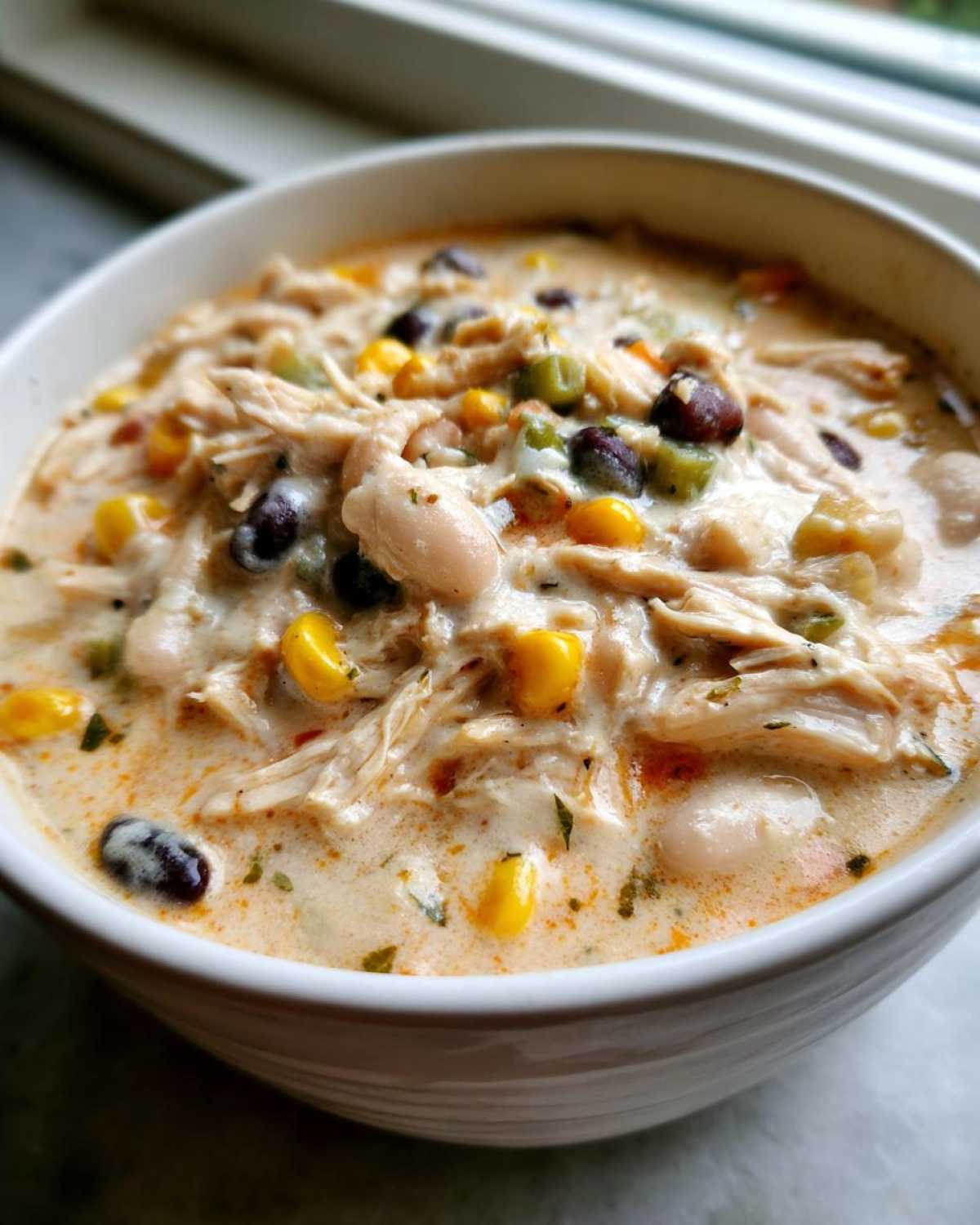 Close-up of a hearty bowl of cream cheese chicken chili, showing shredded chicken, white beans, corn, and black beans in a creamy sauce.