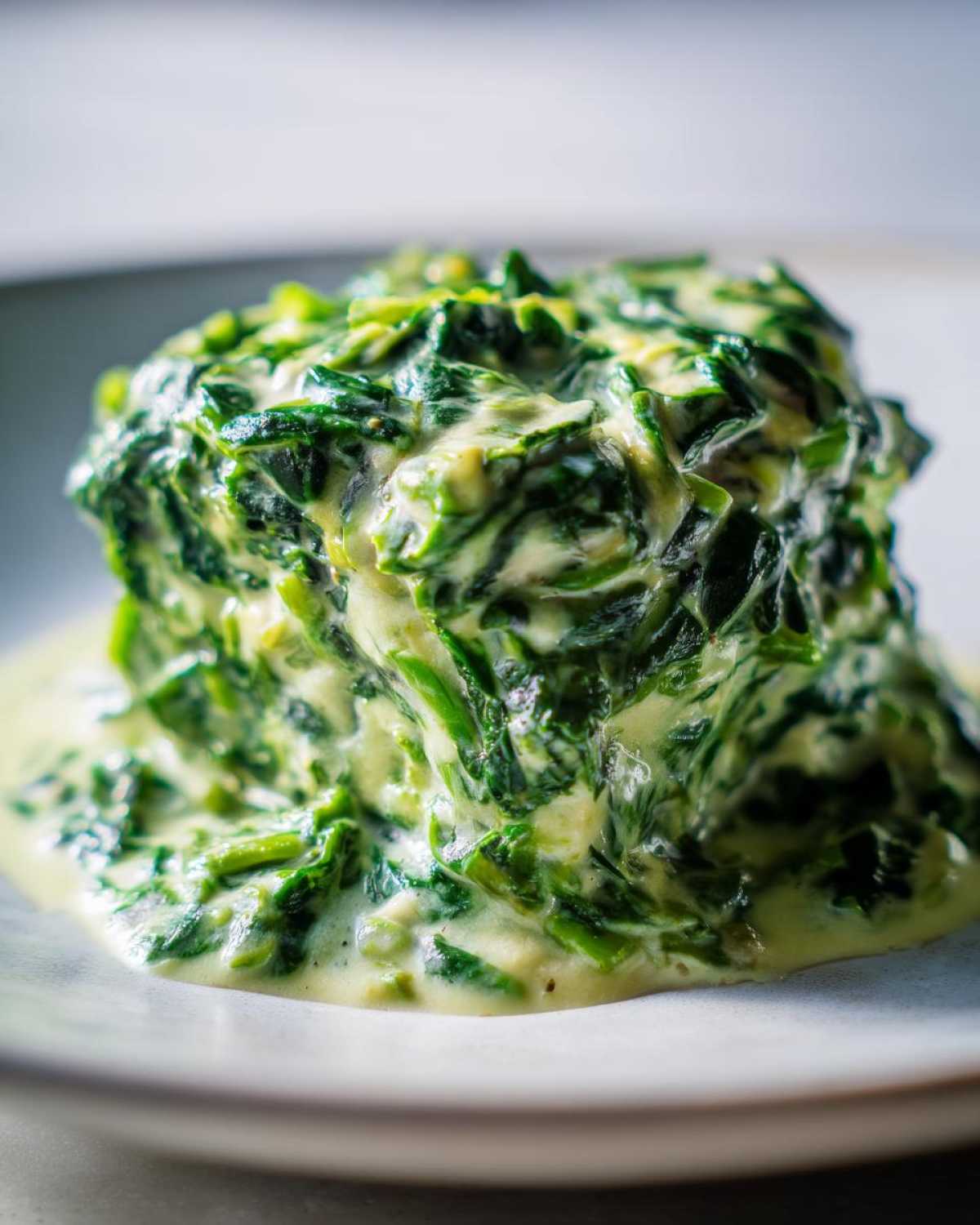A close-up, vertical shot of a mound of rich creamed spinach recipe served on a light plate.