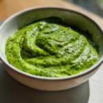 Close-up of a small bowl filled with vibrant, creamy avocado sauce, showing swirls on the surface.