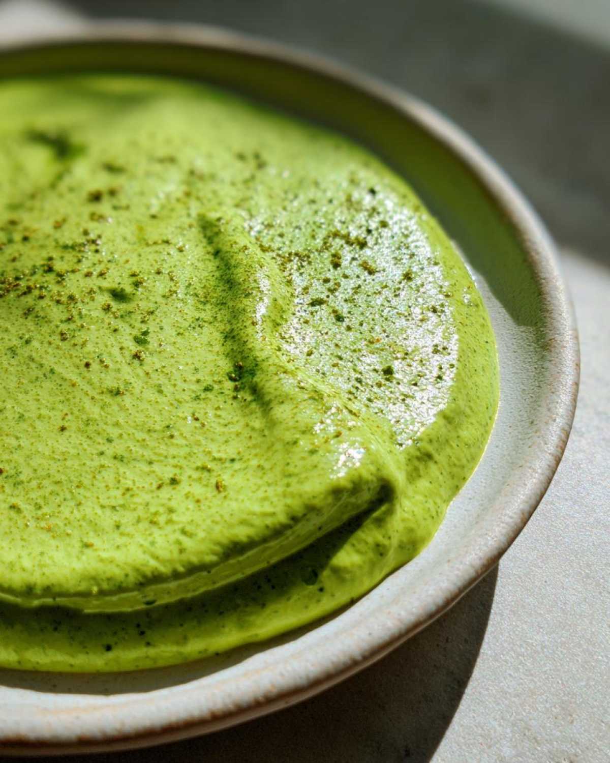 Close-up of thick, vibrant green avocado sauce topped with spices in a rustic bowl.