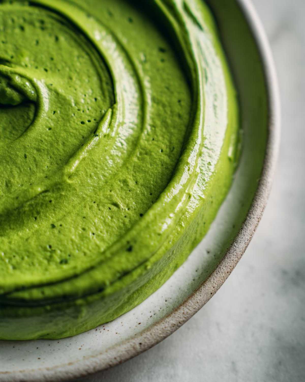 A close-up, top-down view of thick, vibrant green avocado sauce swirled beautifully in a rustic ceramic bowl.