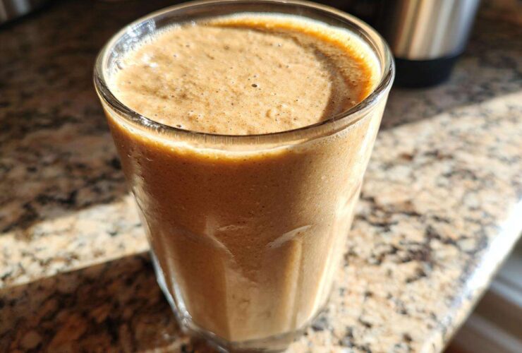 Close-up of a creamy brown banana smoothie in a clear glass sitting on a granite countertop.