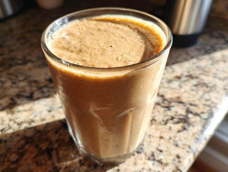 Close-up of a creamy brown banana smoothie in a clear glass sitting on a granite countertop.