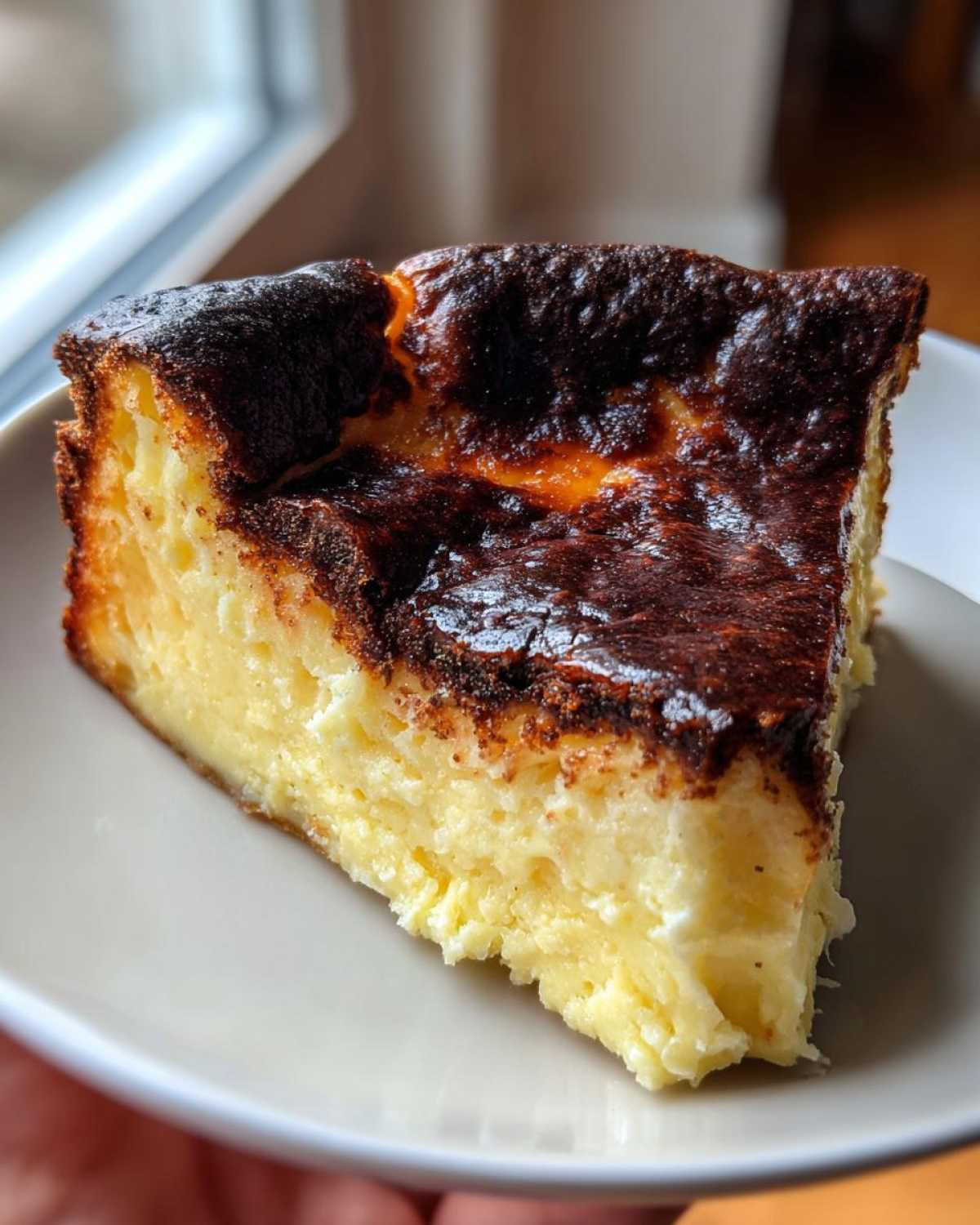 A close-up slice of creamy basque cheesecake showing its signature dark, caramelized top.
