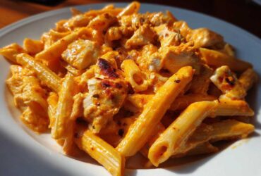 Close-up of creamy, orange-sauced enchilada pasta mixed with chunks of chicken on a white plate.