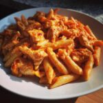 A close-up, appetizing serving of creamy enchilada pasta mixed with chunks of chicken in a white bowl.
